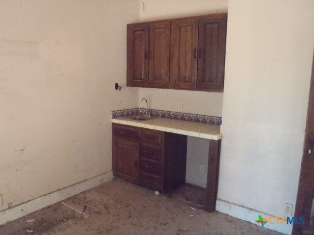 kitchen with tile counters, dark brown cabinetry, and sink