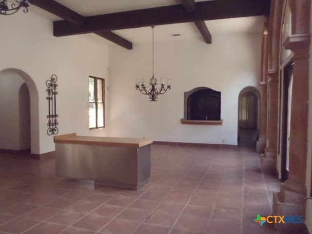 interior space featuring dark tile patterned flooring, beamed ceiling, and a chandelier