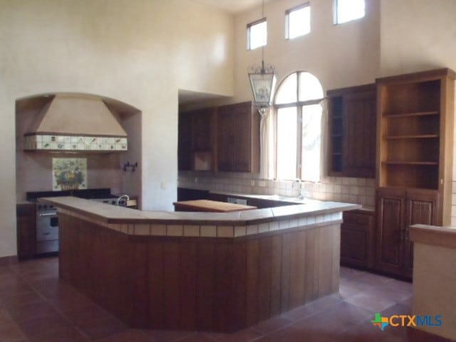 kitchen with tile countertops, decorative backsplash, dark tile patterned floors, a high ceiling, and premium range hood