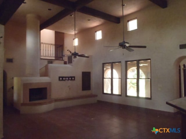 unfurnished living room with ceiling fan, a high ceiling, beam ceiling, and dark hardwood / wood-style floors