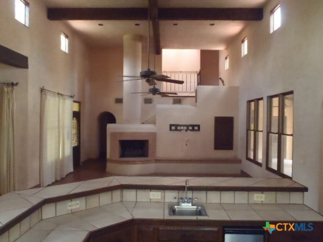 living room featuring a high ceiling, ceiling fan, sink, and beam ceiling