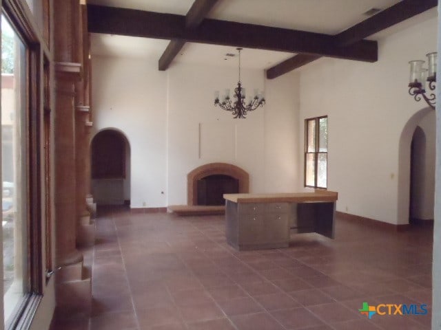 unfurnished living room with a wealth of natural light, a notable chandelier, and beamed ceiling