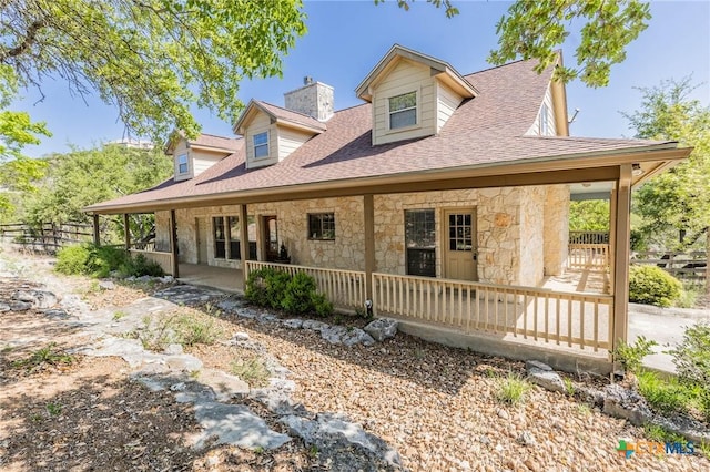 rear view of house featuring a chimney, a shingled roof, fence, and stone siding