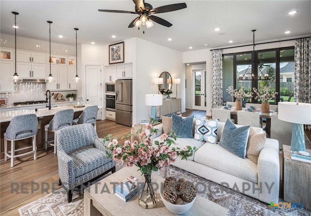 living room with sink, ceiling fan with notable chandelier, light hardwood / wood-style flooring, and a wealth of natural light