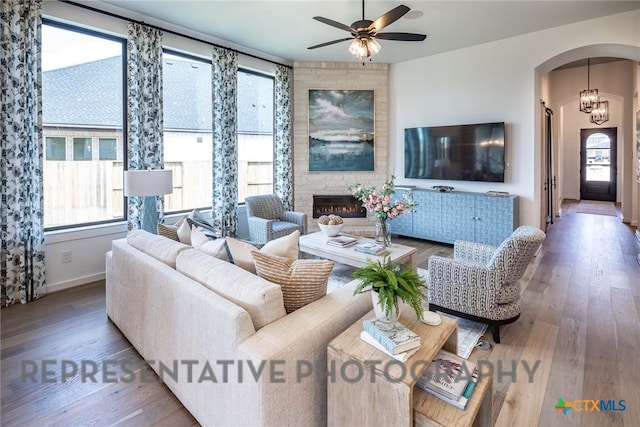 living room with hardwood / wood-style flooring, a large fireplace, and ceiling fan with notable chandelier