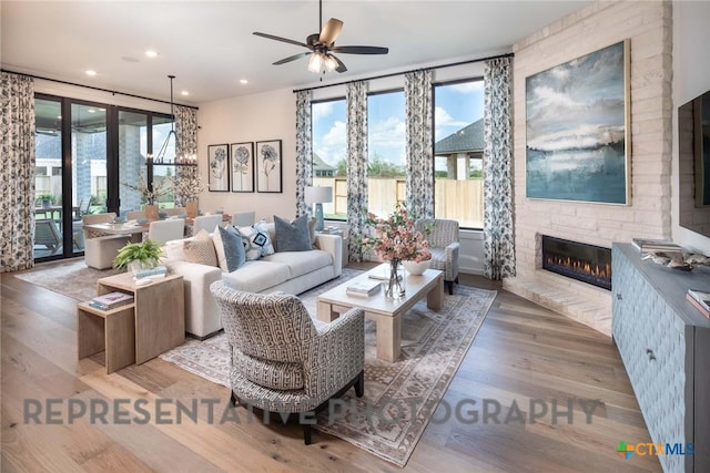 living room featuring a large fireplace, ceiling fan with notable chandelier, and light hardwood / wood-style flooring