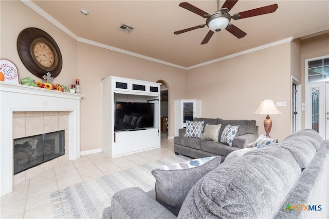 living area featuring arched walkways, light tile patterned floors, a tile fireplace, visible vents, and ornamental molding