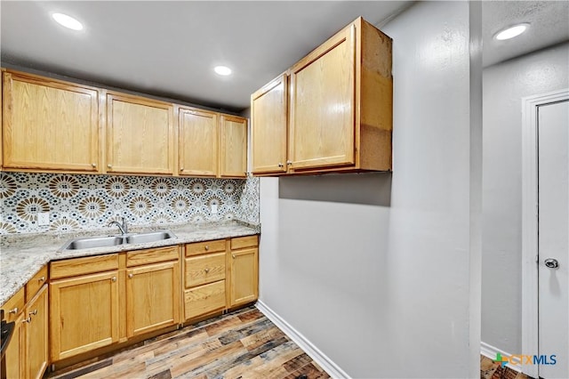 kitchen with a sink, baseboards, light wood-type flooring, light brown cabinetry, and tasteful backsplash