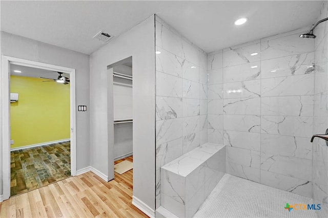 full bath featuring baseboards, visible vents, a ceiling fan, wood finished floors, and a tile shower