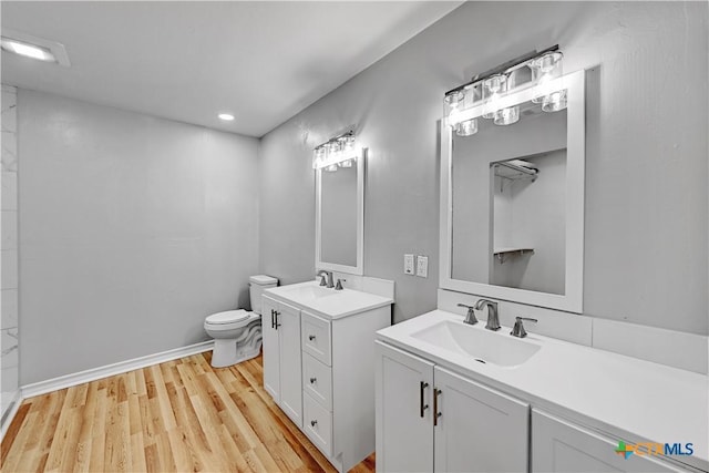 bathroom featuring wood finished floors, two vanities, a sink, and toilet