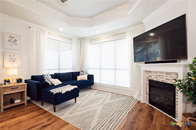 living room with hardwood / wood-style floors, a raised ceiling, crown molding, and a brick fireplace