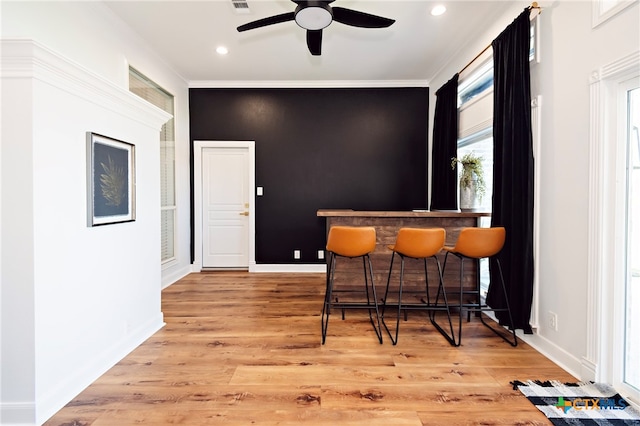 dining area featuring ceiling fan, light wood-type flooring, indoor bar, and ornamental molding