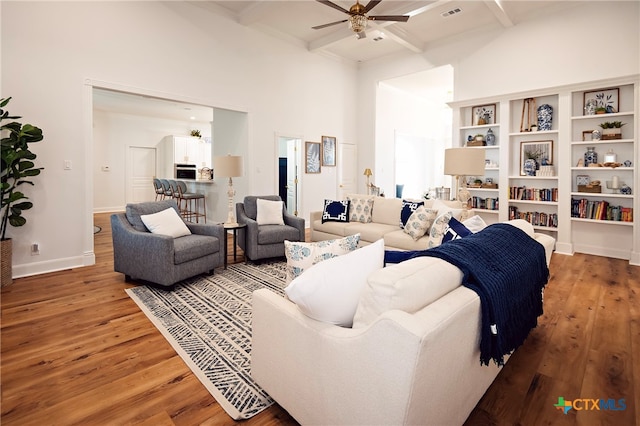 living room featuring a high ceiling, beamed ceiling, hardwood / wood-style flooring, and ceiling fan