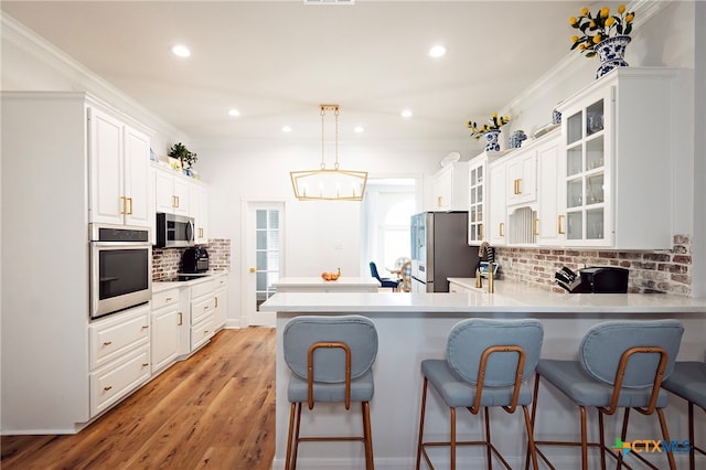 kitchen featuring kitchen peninsula, decorative backsplash, pendant lighting, light wood-type flooring, and appliances with stainless steel finishes