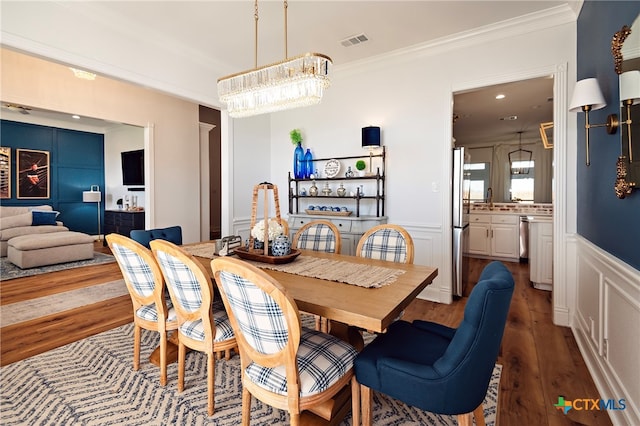 dining area with hardwood / wood-style flooring, sink, an inviting chandelier, and ornamental molding