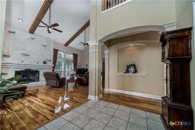 foyer with light tile patterned floors, high vaulted ceiling, a stone fireplace, a ceiling fan, and beamed ceiling