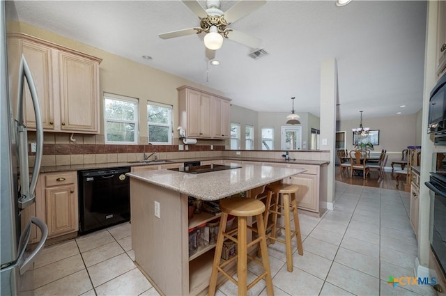 kitchen with a breakfast bar area, light tile patterned floors, light brown cabinetry, a kitchen island, and black appliances