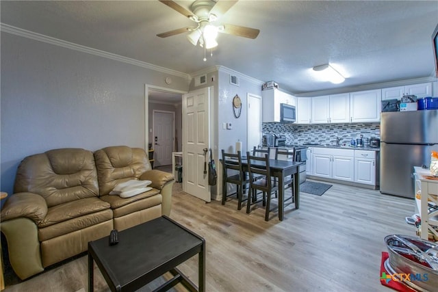 living room featuring ceiling fan, sink, light hardwood / wood-style floors, and ornamental molding