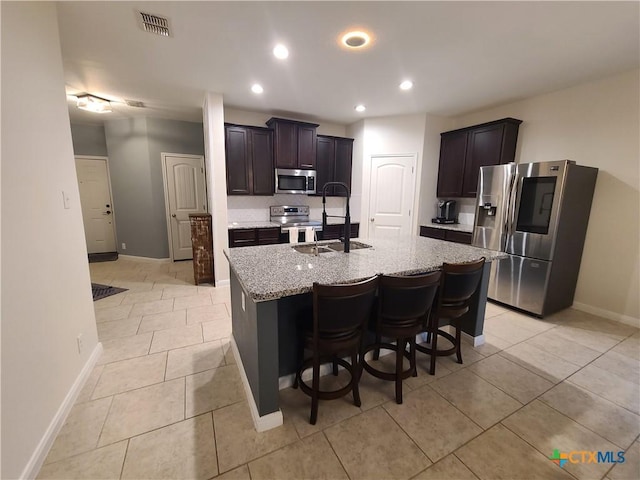 kitchen featuring light stone counters, a breakfast bar, stainless steel appliances, sink, and a center island with sink