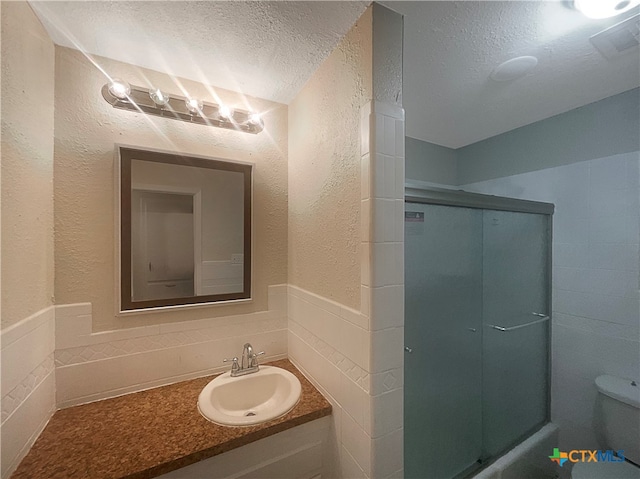 bathroom featuring toilet, vanity, an enclosed shower, and a textured ceiling