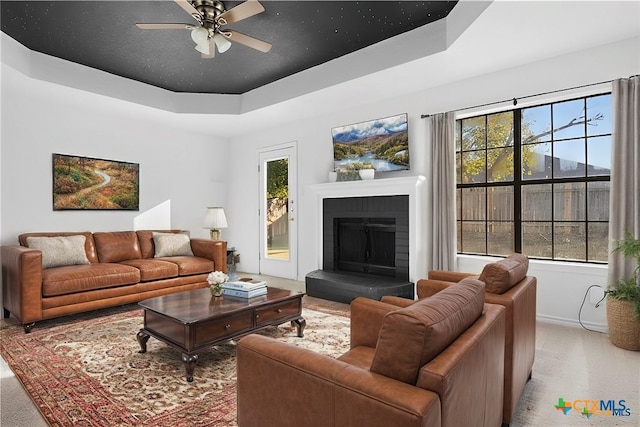 living room featuring a tray ceiling, a wealth of natural light, a fireplace, and ceiling fan