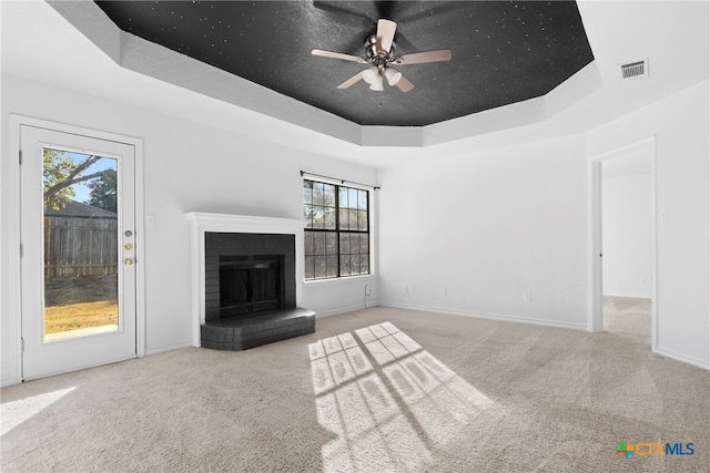 unfurnished living room featuring a brick fireplace, a healthy amount of sunlight, and a tray ceiling