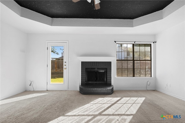 unfurnished living room featuring a tray ceiling, ceiling fan, a fireplace, and light colored carpet