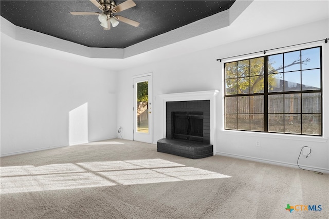 unfurnished living room with a tray ceiling, ceiling fan, carpet, and a brick fireplace