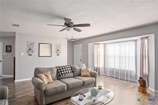 living room featuring wood-type flooring, a textured ceiling, and ceiling fan