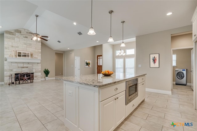 kitchen with a wealth of natural light, washer / clothes dryer, visible vents, stainless steel microwave, and a stone fireplace