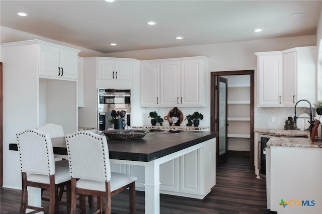 194 Panorama Ln, Victoria, TX 77905 - kitchen with stainless steel double oven, a sink, white cabinetry, dark wood-style floors, and backsplash