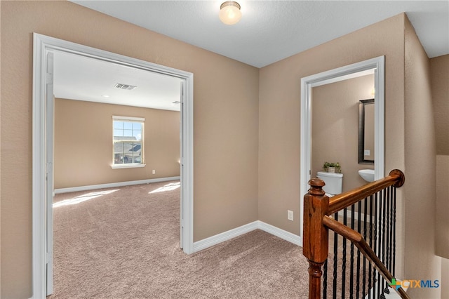 hall featuring baseboards, an upstairs landing, and carpet flooring