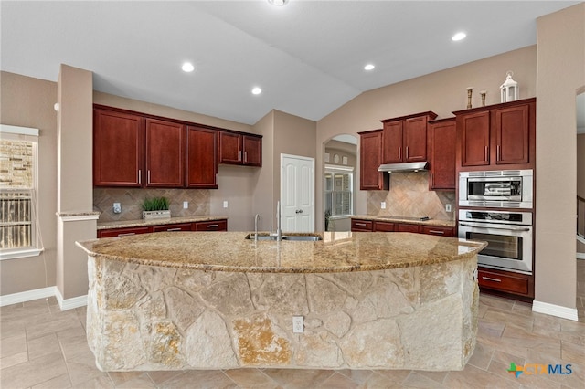 kitchen with under cabinet range hood, a sink, arched walkways, appliances with stainless steel finishes, and lofted ceiling