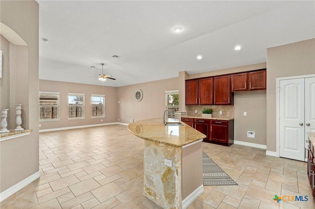 kitchen with light stone counters, a ceiling fan, baseboards, and a sink