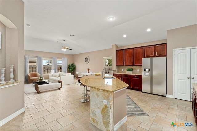 kitchen with light stone countertops, open floor plan, a breakfast bar area, stainless steel fridge, and a sink