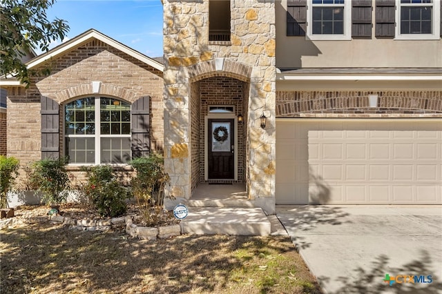 view of exterior entry with brick siding, stone siding, driveway, and a garage