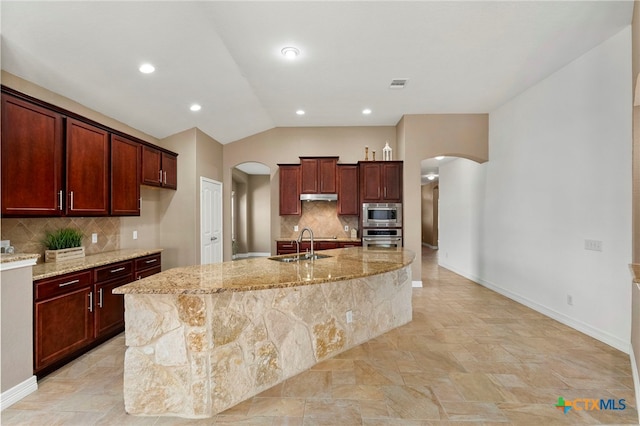 kitchen with visible vents, light stone countertops, arched walkways, stainless steel appliances, and a sink