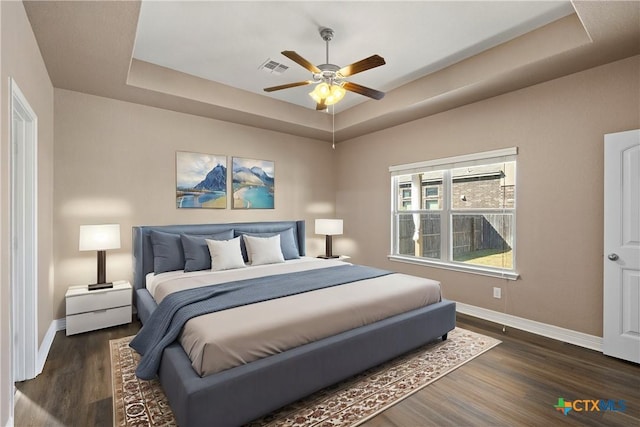 bedroom featuring a tray ceiling, baseboards, and dark wood-style flooring