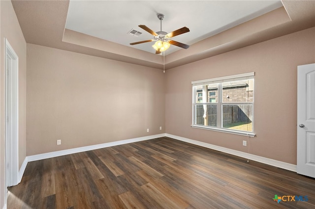 empty room with baseboards, a raised ceiling, dark wood-type flooring, and a ceiling fan