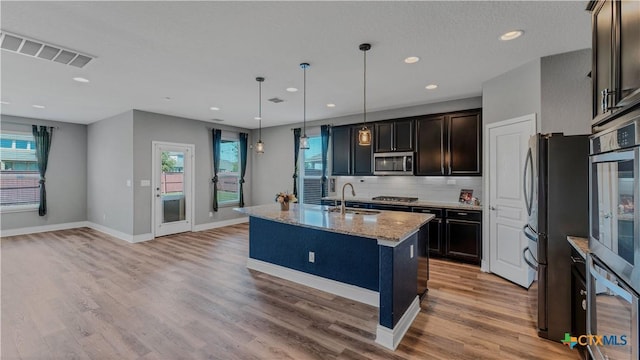 kitchen featuring visible vents, a sink, tasteful backsplash, stainless steel appliances, and light stone countertops