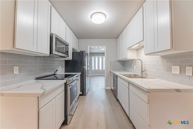 kitchen with light wood finished floors, decorative backsplash, light stone countertops, stainless steel appliances, and a sink