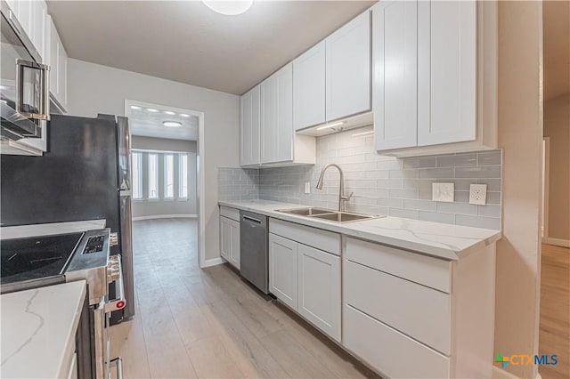 kitchen featuring light wood-style flooring, decorative backsplash, appliances with stainless steel finishes, white cabinetry, and a sink