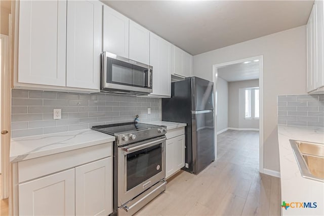 kitchen with appliances with stainless steel finishes, white cabinets, light wood-style floors, and light stone countertops