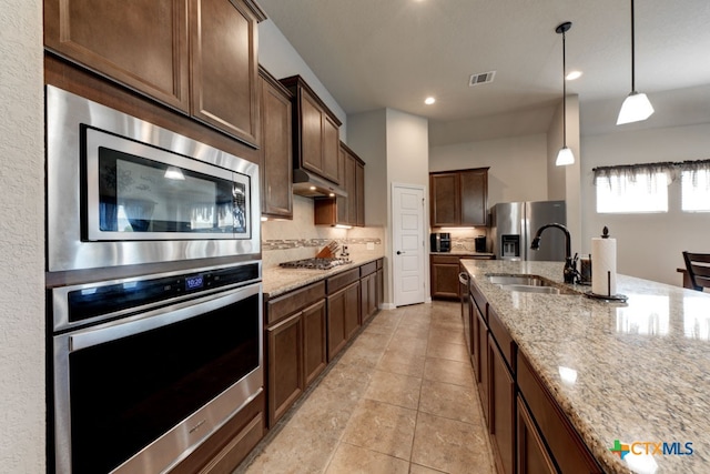 kitchen featuring stainless steel appliances, sink, pendant lighting, and light stone counters