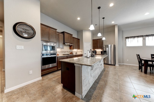 kitchen with stainless steel appliances, a center island with sink, a breakfast bar, light stone counters, and decorative light fixtures