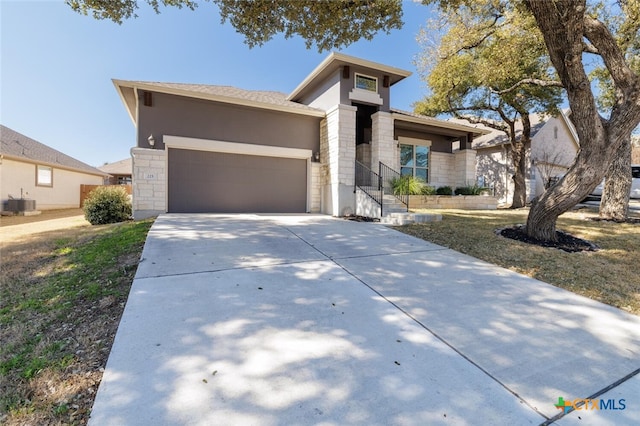 prairie-style home featuring an attached garage, central AC, stone siding, concrete driveway, and stucco siding