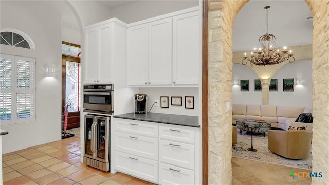 680 Saddleridge Dr, Wimberley, TX 78676 - kitchen featuring arched walkways, light tile patterned floors, beverage cooler, white cabinetry, and oven