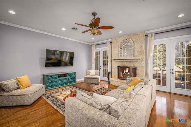 living room with french doors, a stone fireplace, crown molding, hardwood / wood-style flooring, and ceiling fan