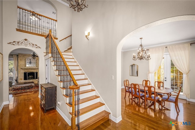 staircase featuring an inviting chandelier, a healthy amount of sunlight, a stone fireplace, and hardwood / wood-style flooring