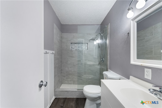 bathroom featuring a tile shower, a textured ceiling, toilet, vanity, and hardwood / wood-style flooring